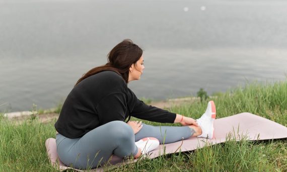 A woman stretches on a yoga mat by a serene lake, embodying relaxation and wellness in nature.